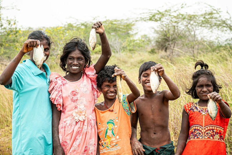 Five village children laughing together in a dry grassy field