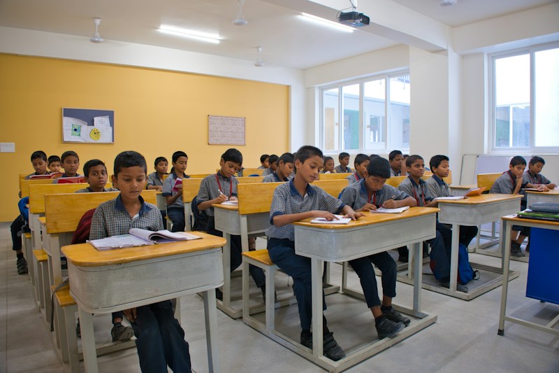 Rows of students at yellow desks in a bright classroom
