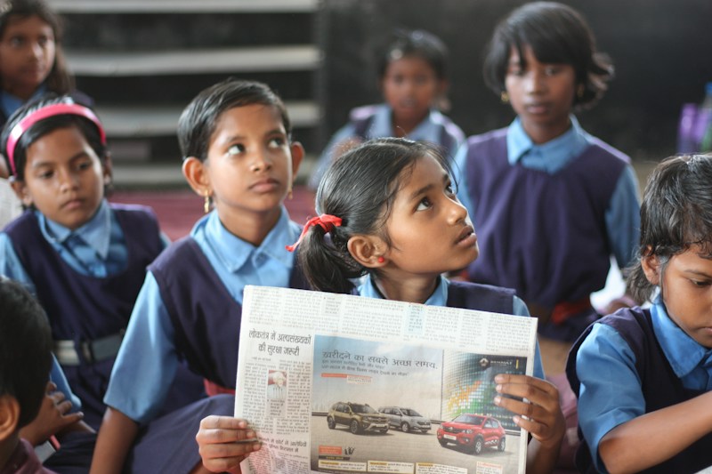 A curious young girl in school uniform reading a newspaper among her classmates