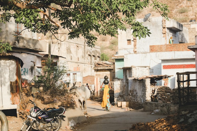 A quiet village lane with homes, a parked motorbike and a woman walking